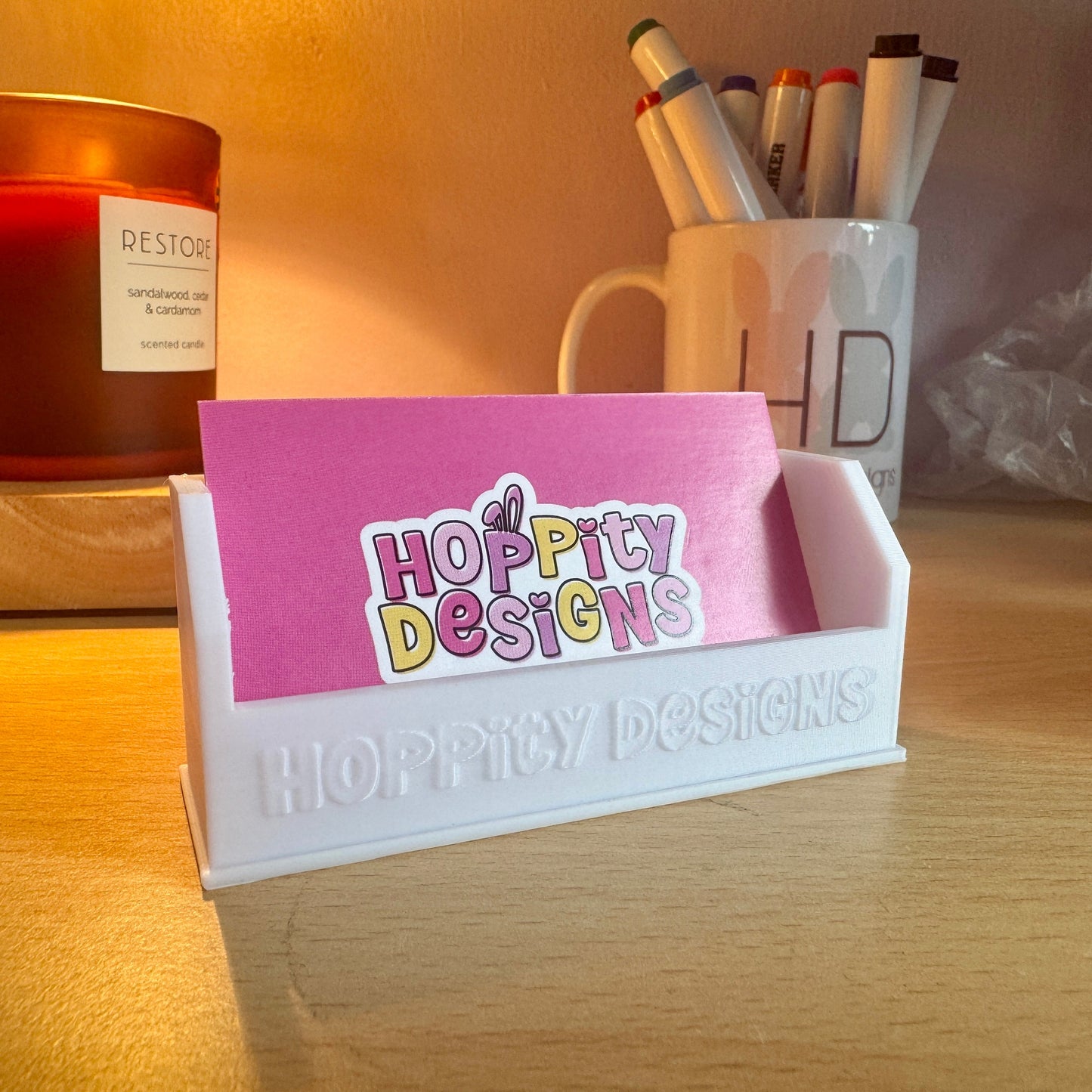 Desk setup with a pink card holder displaying 'Hoppy Designs' on a wooden surface.