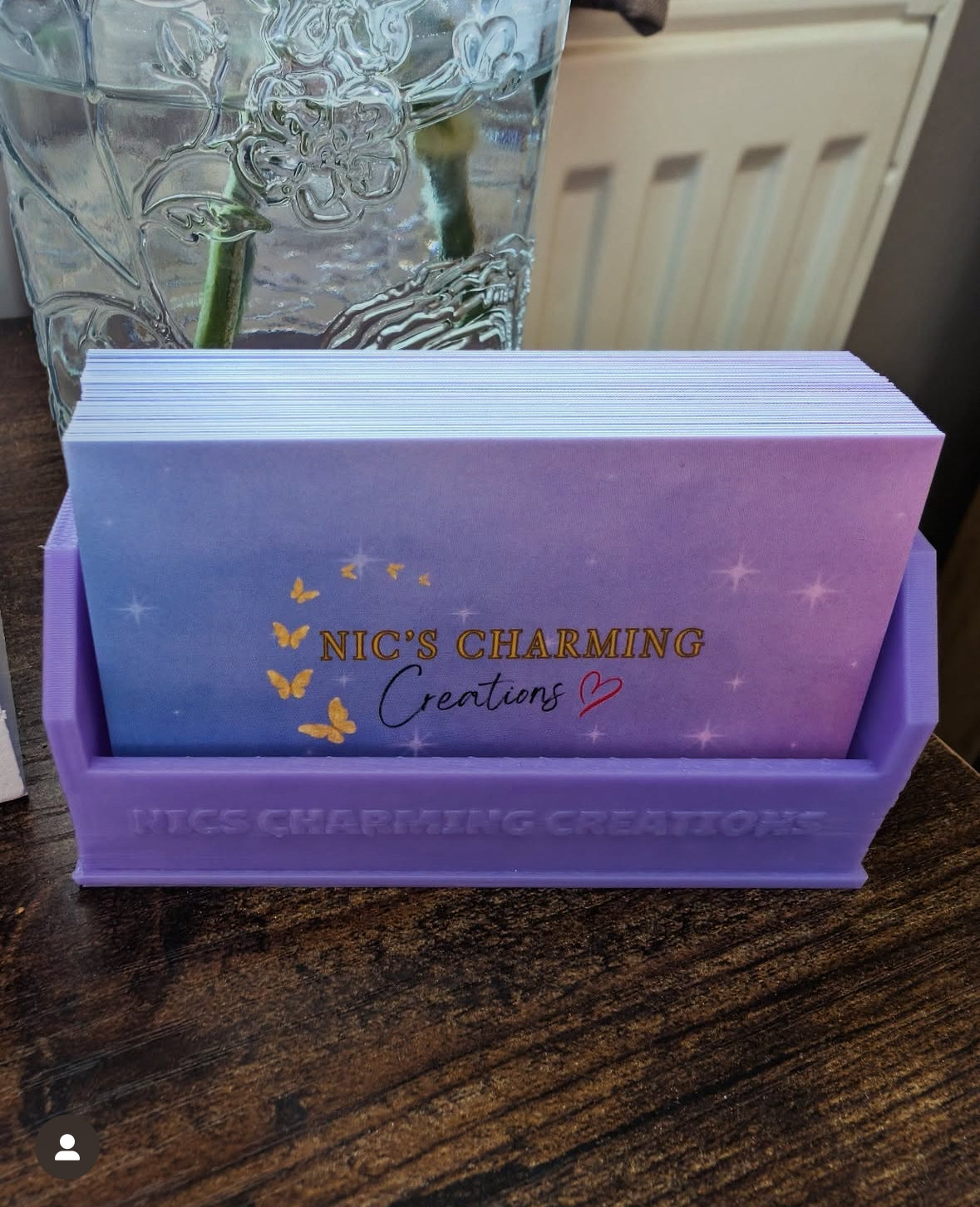 Stack of cards with 'Nic's Charming Creations' branding in a purple holder on a wooden surface.