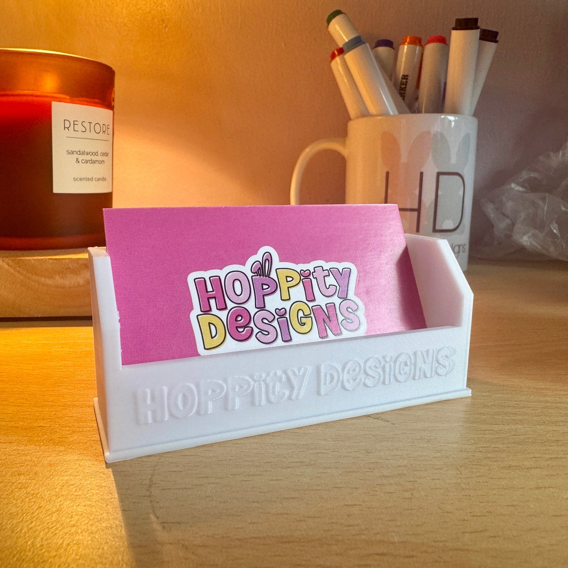 Desk setup with a pink card holder displaying 'Hoppy Designs' on a wooden surface.