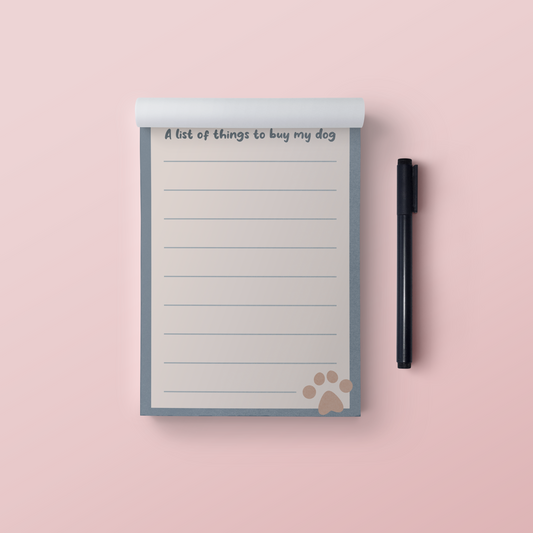 A picture of a Blue and cream notepad that says A list of things to buy my dog at the top with a brown paw print in the bottom right hand corner. Pictured on a pink background with a black pen next to it.