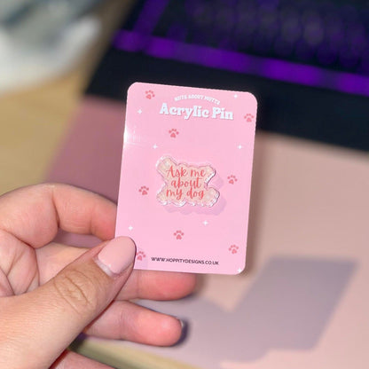 Lady with pink nails holding an acrylic pin that says ask me about my dog, mounted onto a pink backing card with a rgb keyboard in the background.